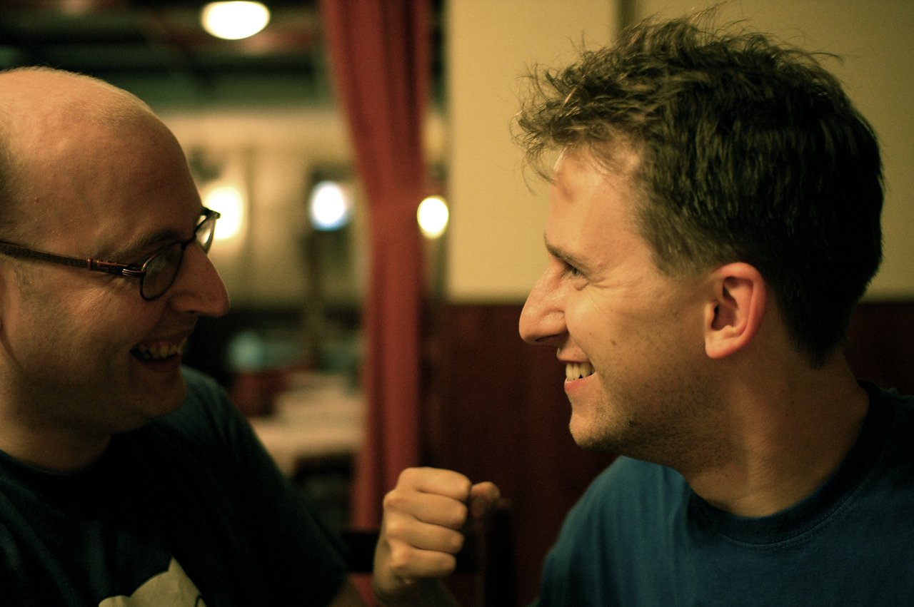 Two men smiling at each other, one playfully raising a fist in a friendly gesture.