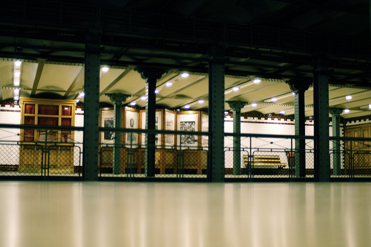 A well-lit metro station with benches, framed pictures, and decorative columns, viewed from a low angle.
