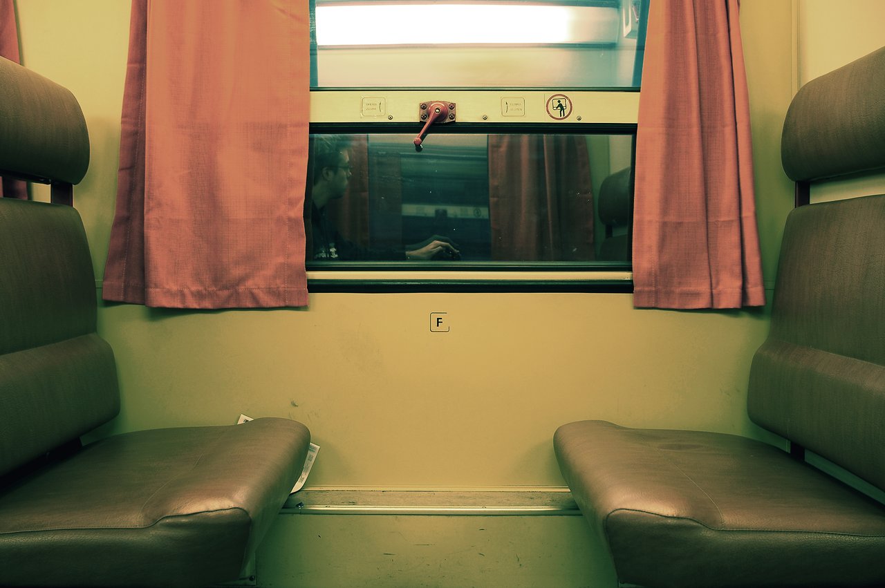 Empty train compartment with two brown seats and a window reflecting a person sitting outside.