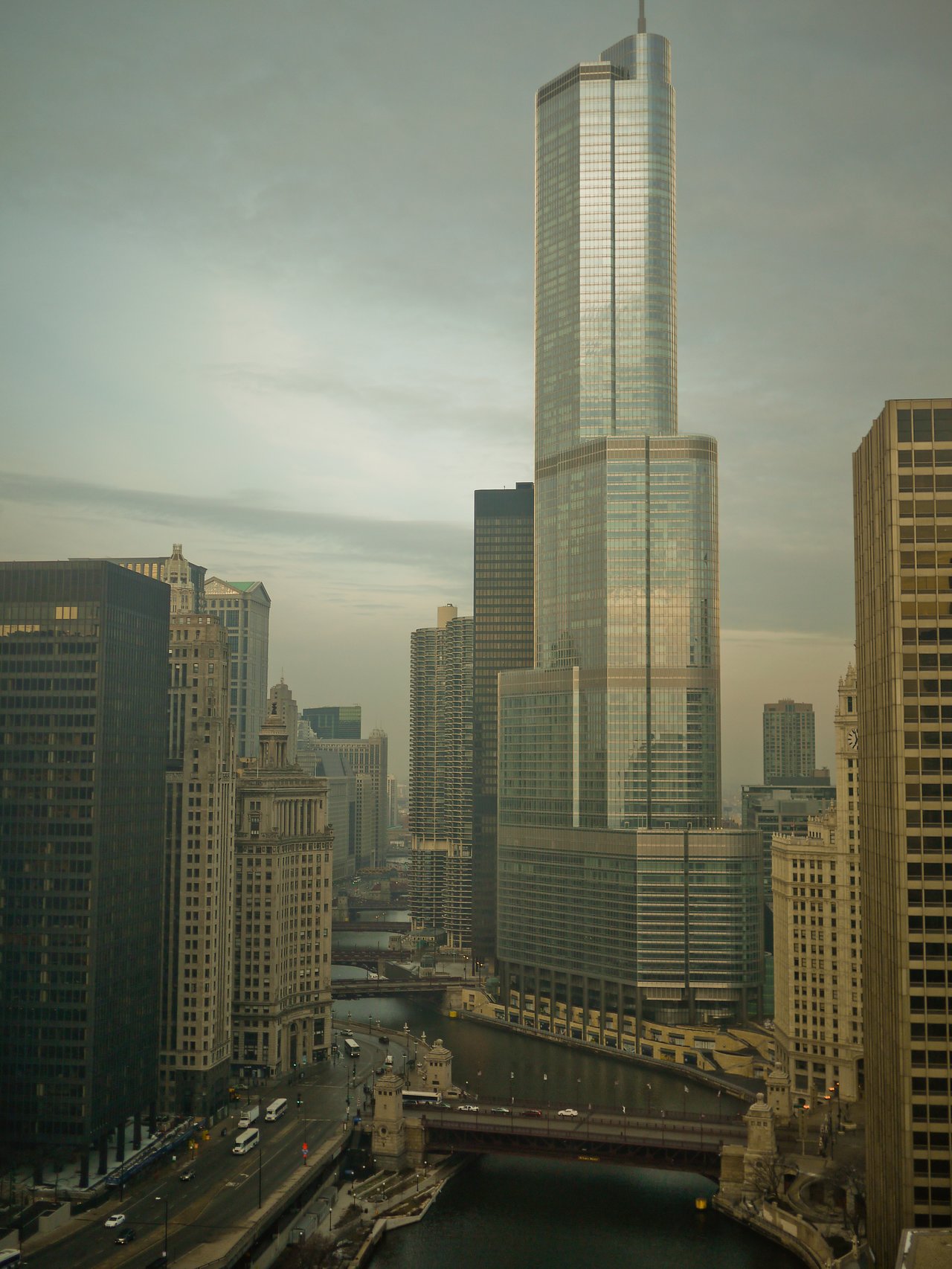A cityscape of Chicago featuring a tall glass skyscraper, surrounding buildings, and a river with bridges.