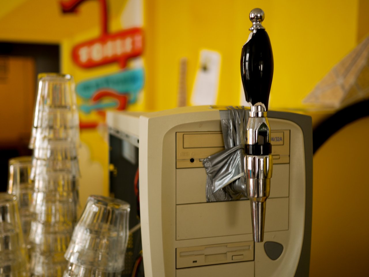 A beer tap handle is duct-taped to the front of an old beige computer tower.