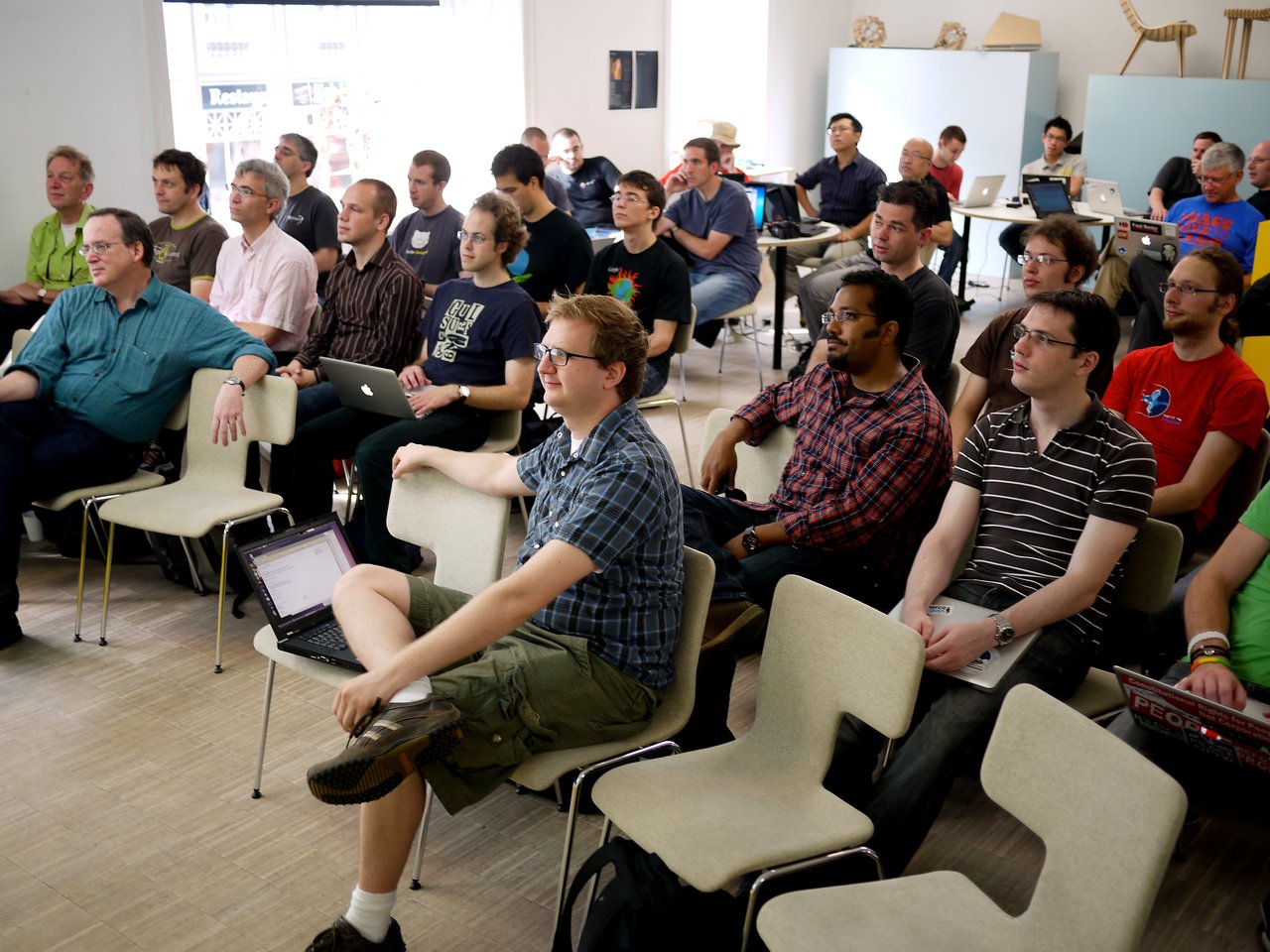 A group of people attentively listen during a DrupalCon Copenhagen 2010 code sprint, with laptops open.