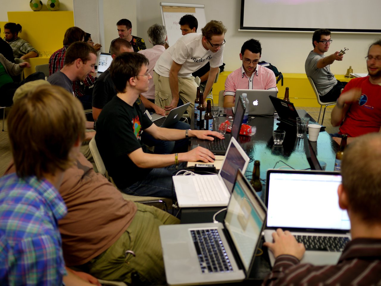 A group of people working on laptops during a coding sprint, collaborating and discussing at a conference table.