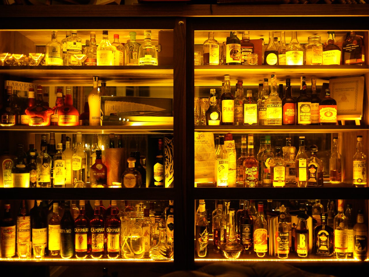 A well-lit bar shelf displaying a variety of liquor bottles arranged neatly in glass cabinets.