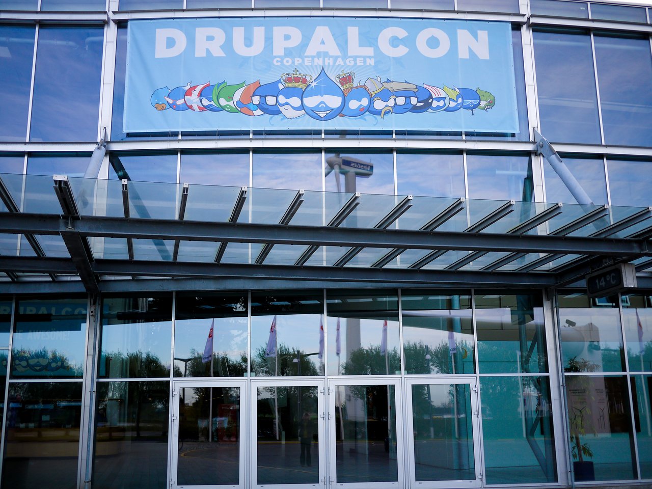 Entrance to a modern glass building with a large "Drupalcon Copenhagen" banner displayed above the doors.