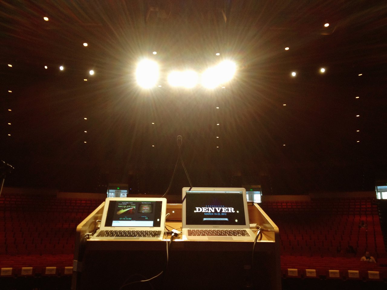 View from a keynote speaker's podium with two laptops displaying DrupalCon Denver 2012 content in a large auditorium.