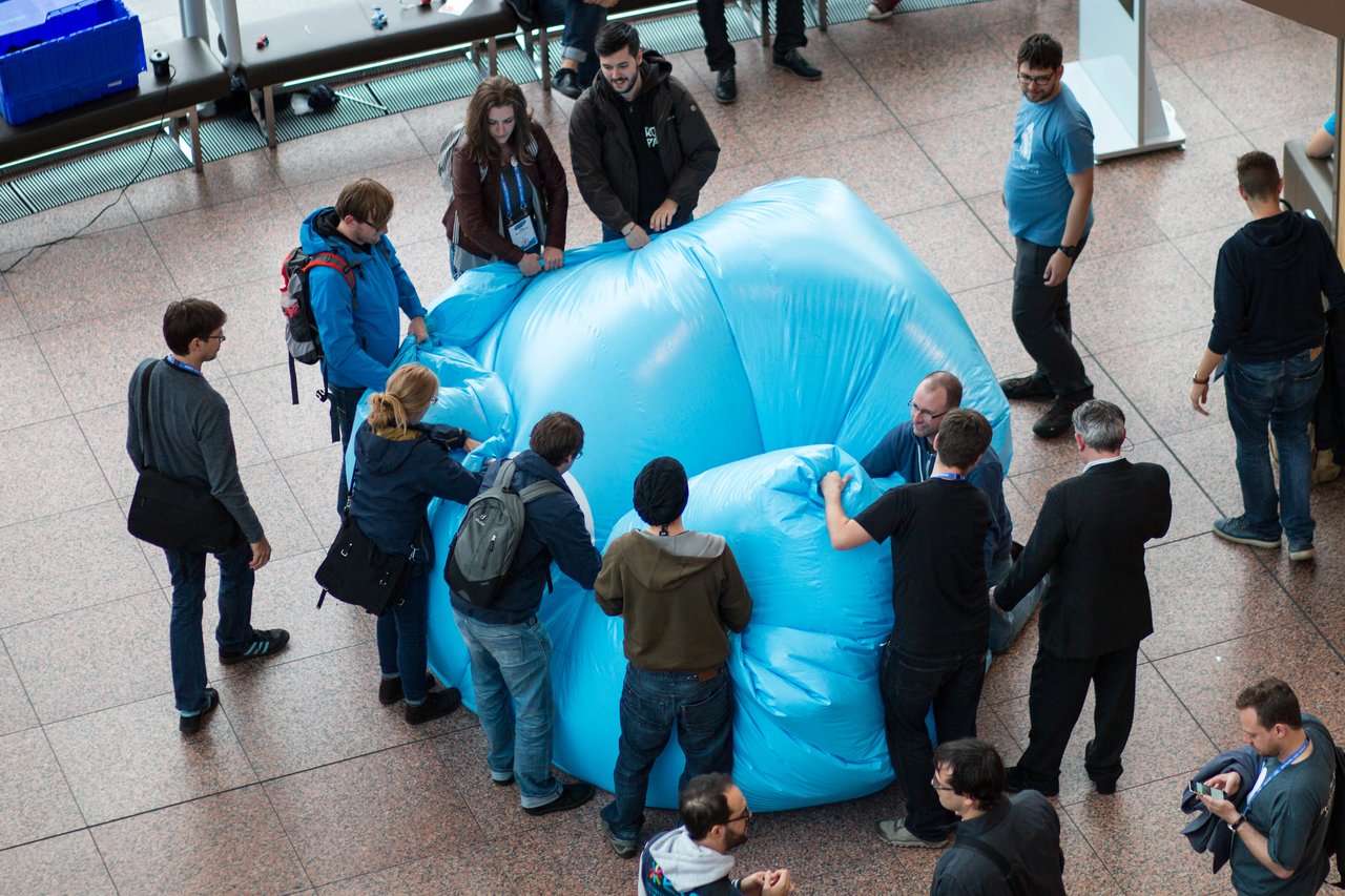 A group of people folds a large, blue inflatable Druplicon at DrupalCon Dublin 2016.