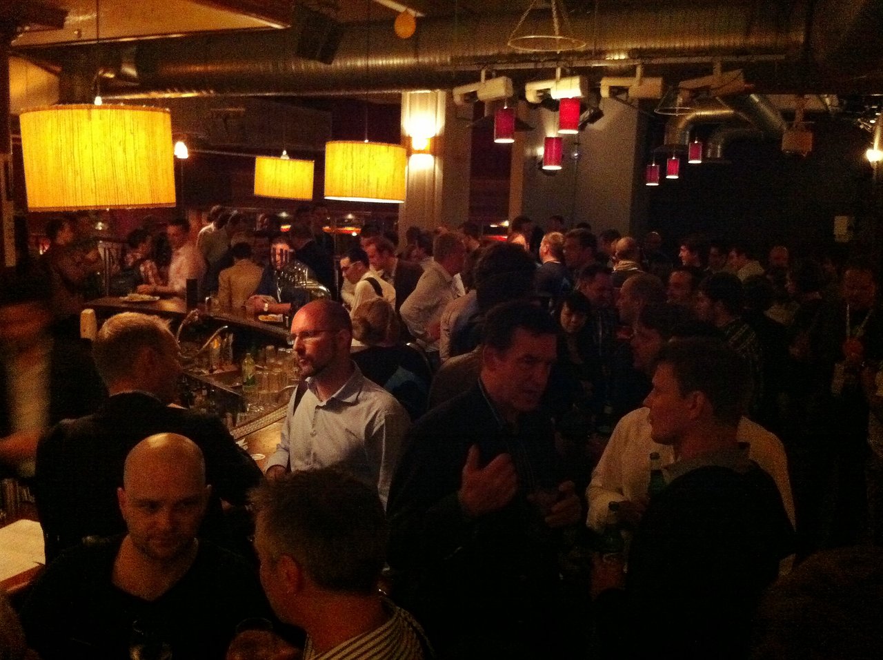 A crowded bar with people socializing, drinking, and engaging in conversations at the Acquia customer party.