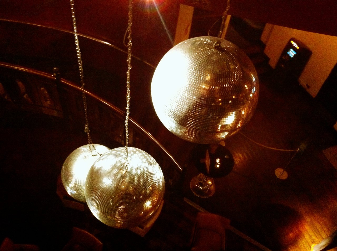 Large disco balls hang from the ceiling, reflecting warm light in a dimly lit party setting.