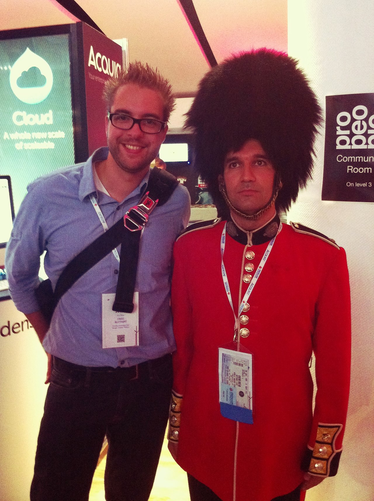 A smiling man in a conference badge stands next to a serious-looking person dressed as a British guard.