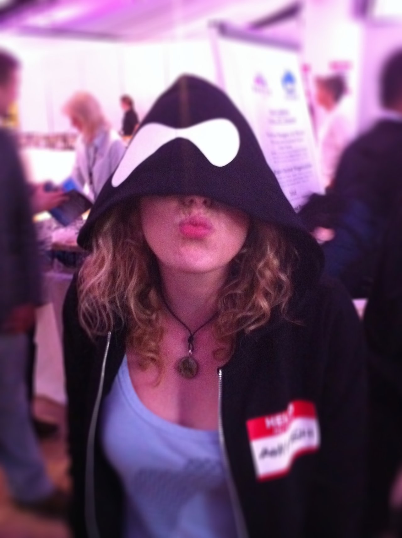 A person wearing a black Drupal hoodie with the hood up, puckering their lips playfully at the camera.