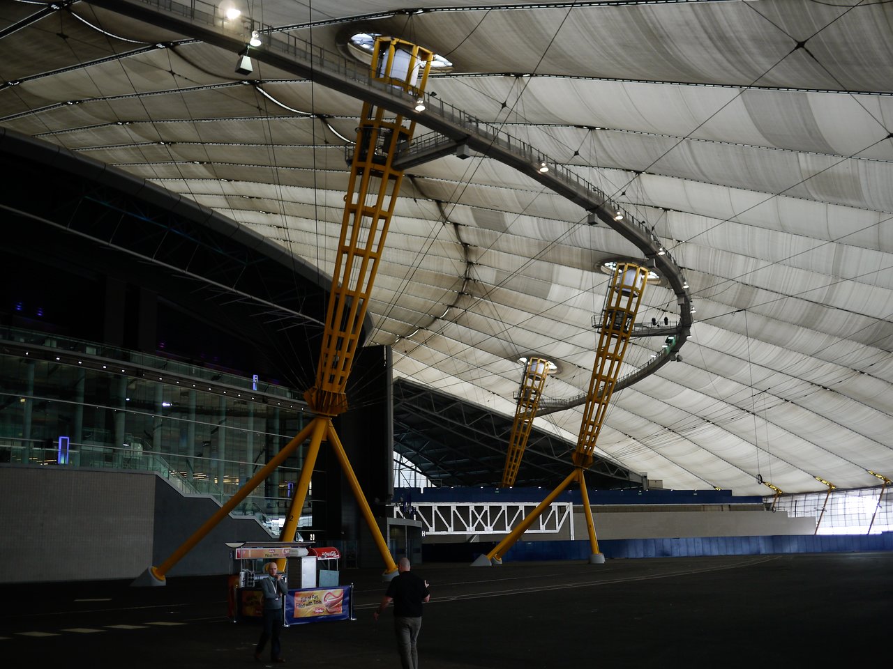Large indoor structure with a white fabric roof, yellow support beams, and a food cart in the foreground.