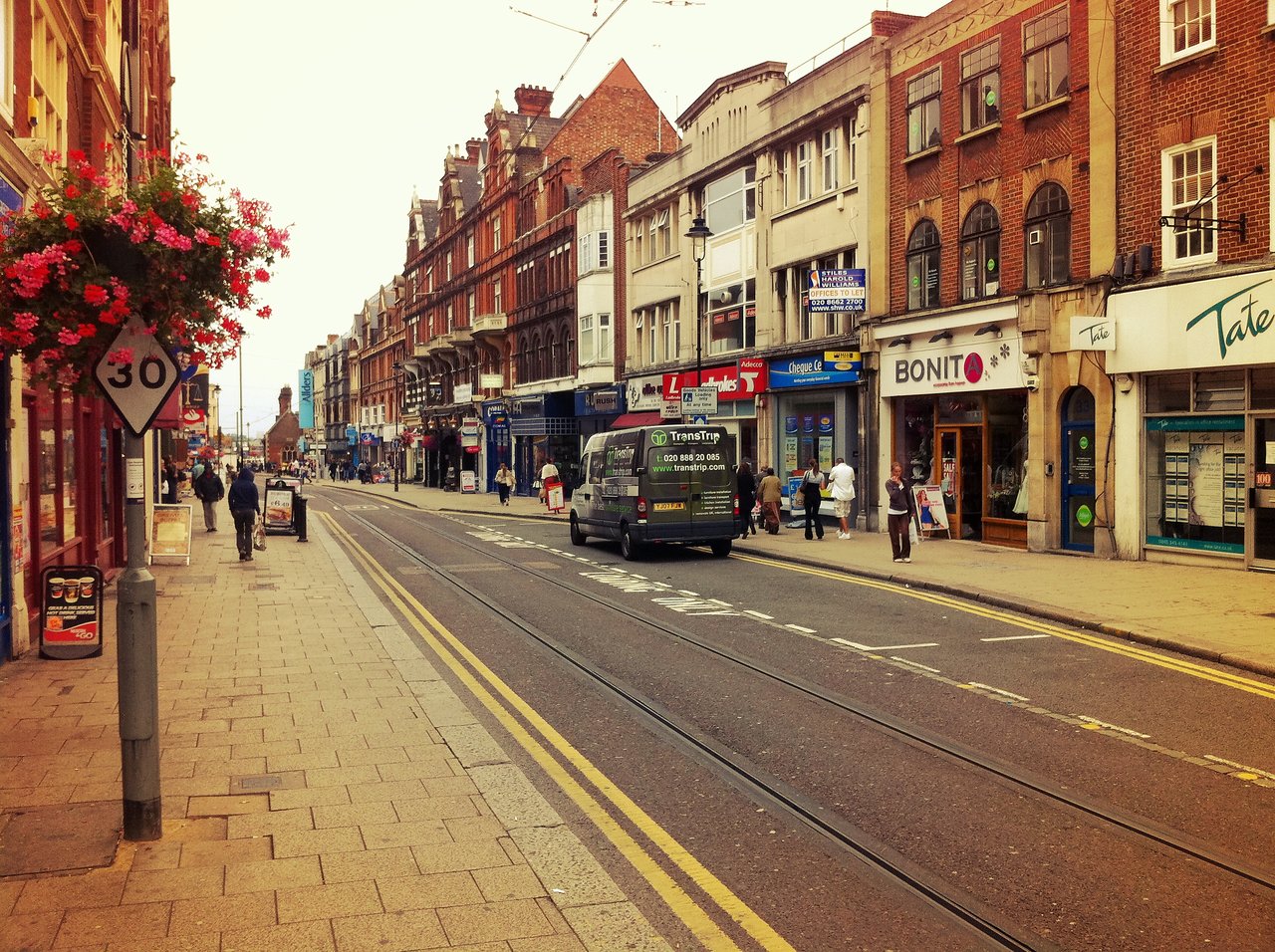 A busy street in Croydon with pedestrians walking on the sidewalk and a bus driving down the road.