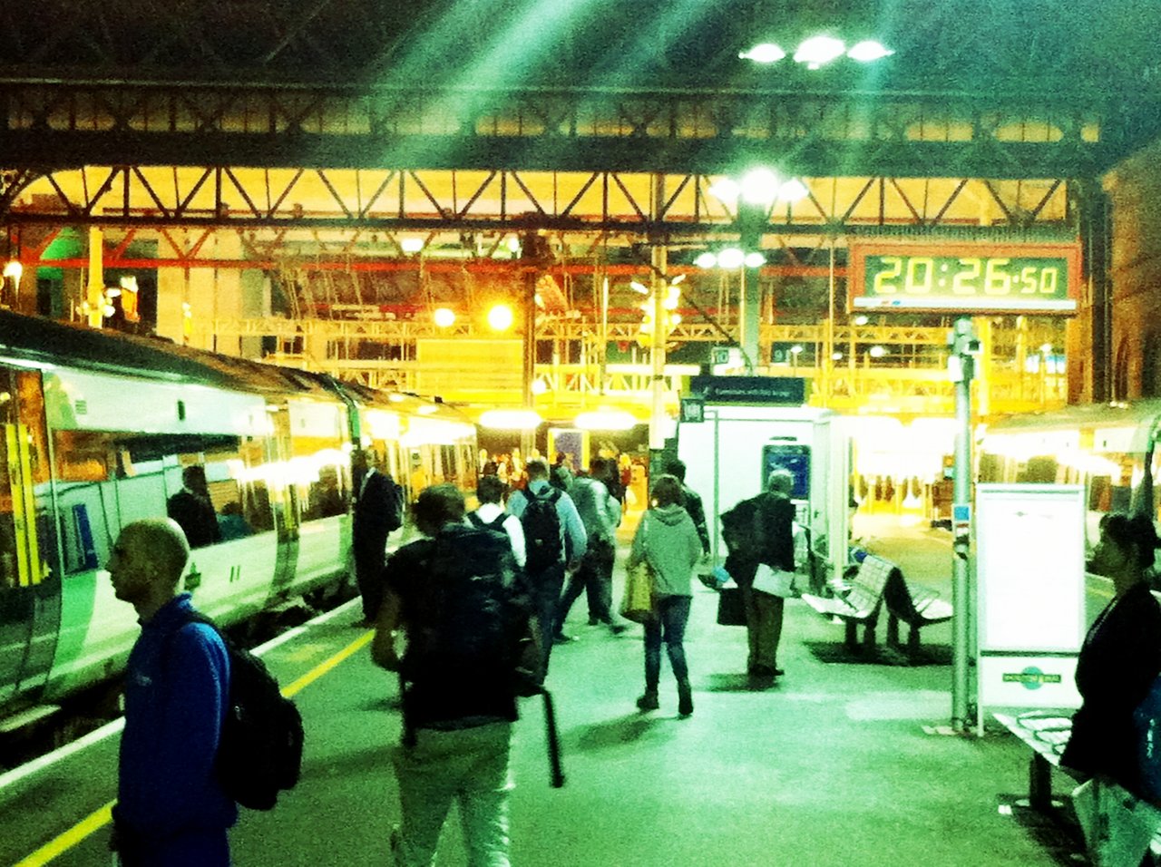 Busy train station with passengers walking along the platform, some carrying bags.