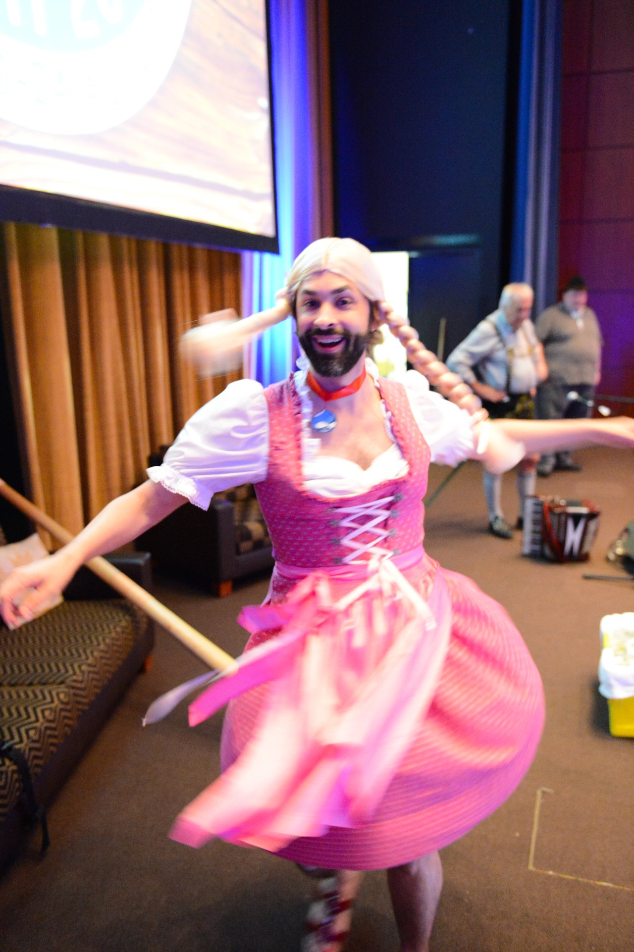 A person in a pink dress and wig spins energetically on stage during an intro session at DrupalCon Munich 2012.