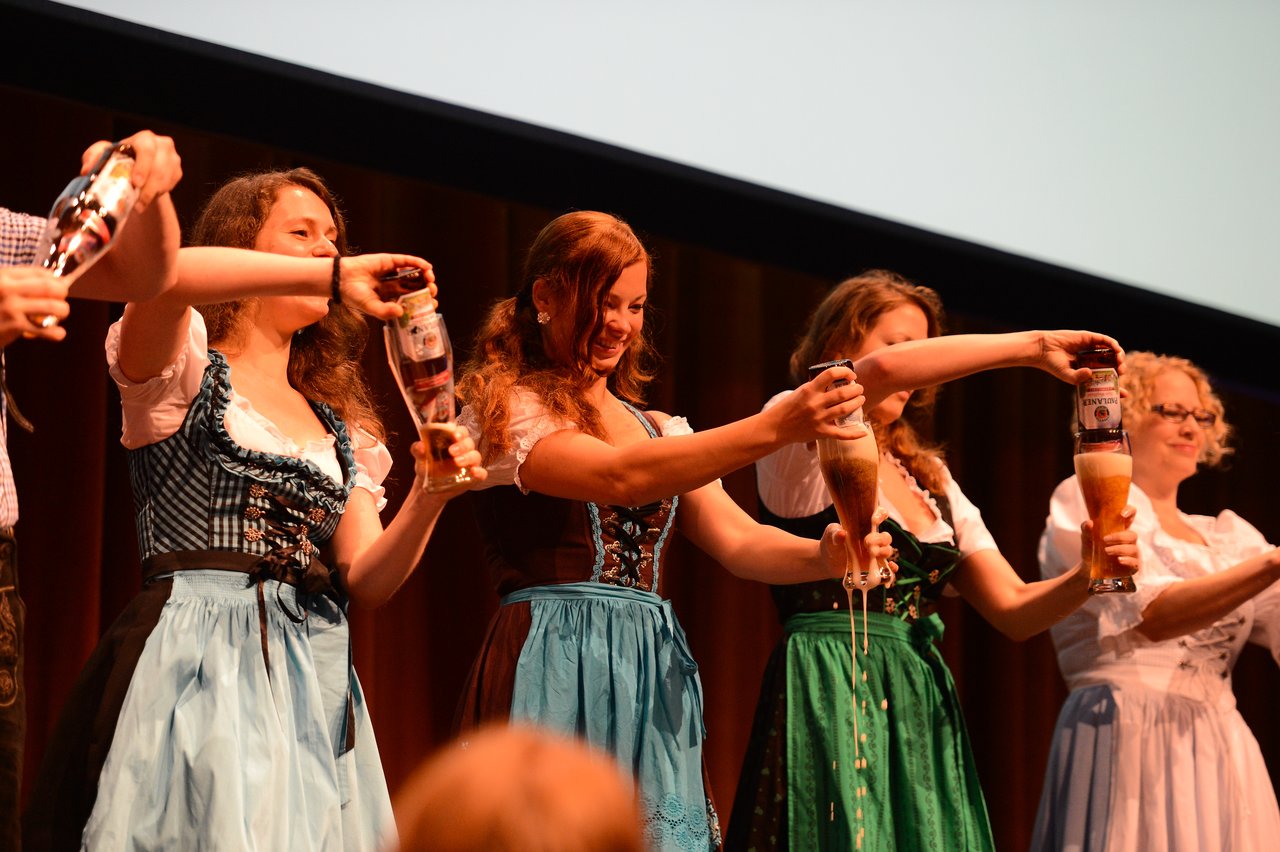 Several women in traditional Bavarian dresses pour beer into glasses on stage during an intro session at DrupalCon Munich.