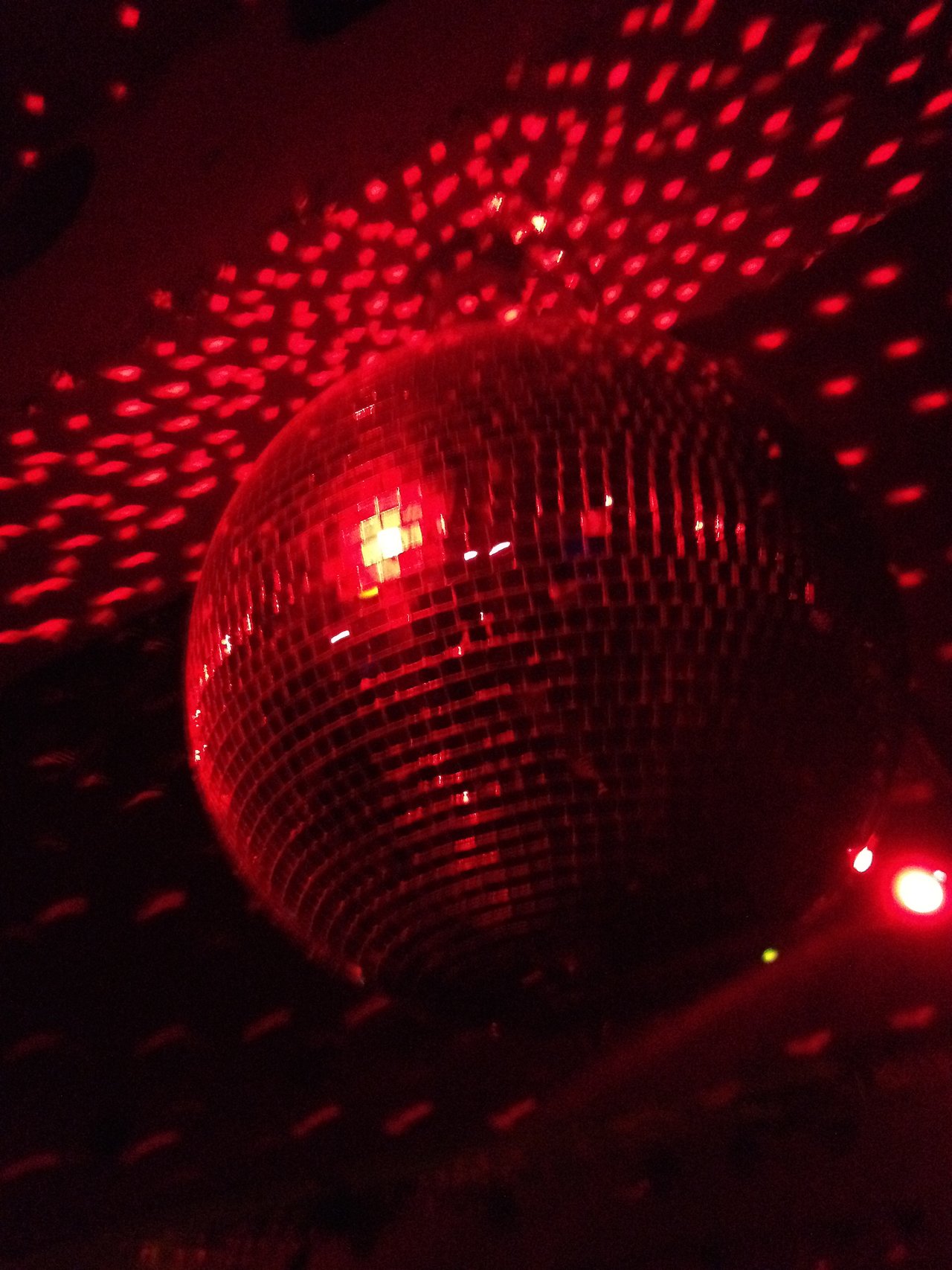 A disco ball reflects red lights in a dark party setting.
