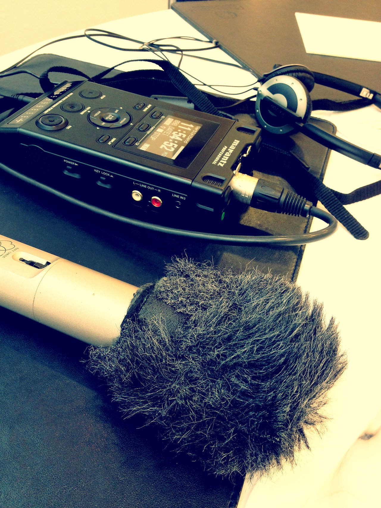 A microphone with a windscreen, an audio recorder, and headphones set up for a radio interview.