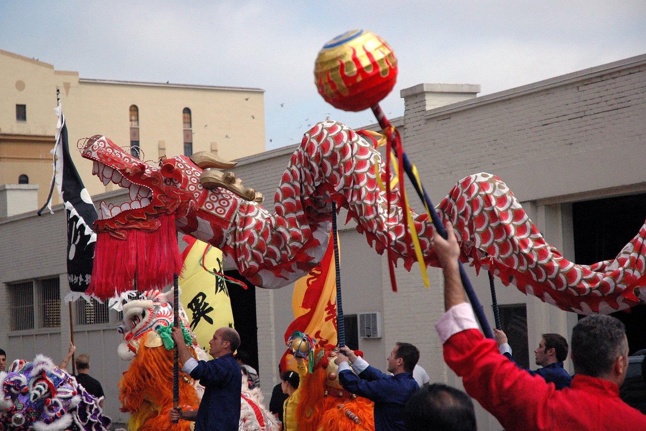 Performers in blue and red outfits manipulate a large red and gold dragon puppet during a Chinatown festival parade.