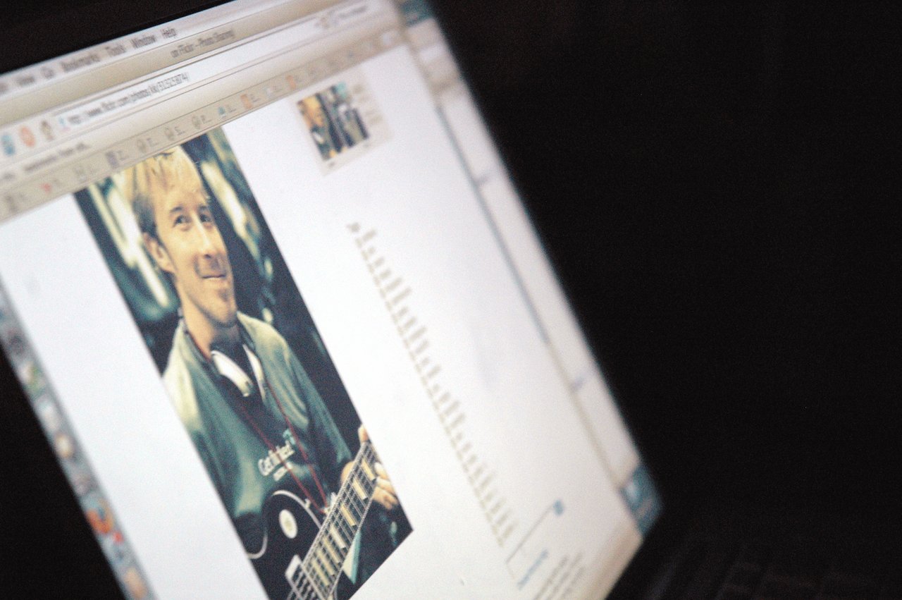 A laptop screen displays a webpage with a photo of a person holding a guitar and wearing headphones.