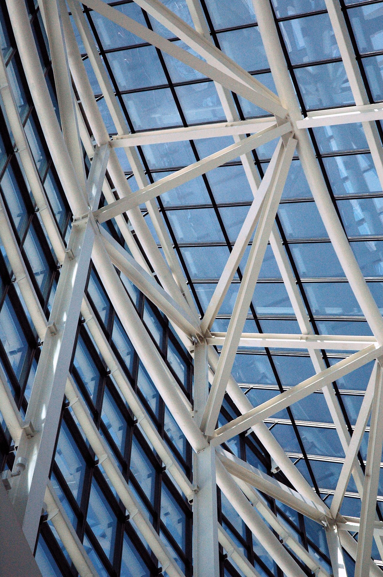 Glass and steel ceiling structure of a convention center, showing intersecting beams and large windows letting in natural light.