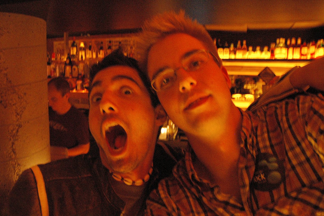 Two people posing for a selfie in a dimly lit bar, one making a playful open-mouthed expression.