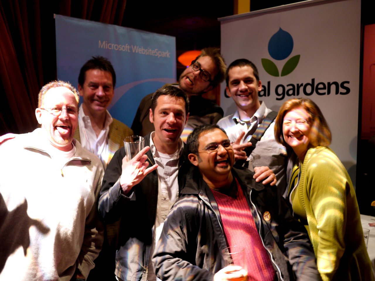 A group of people smiling and posing together at a DrupalCon San Francisco 2010 event with Acquia and Microsoft banners.