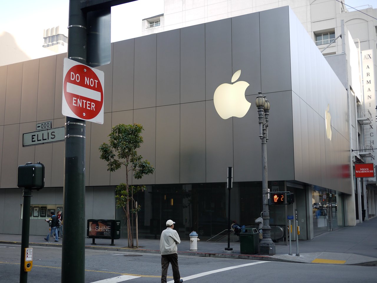 A large Apple Store building with reflective panels and glowing Apple logos on the facade, located at a street corner.