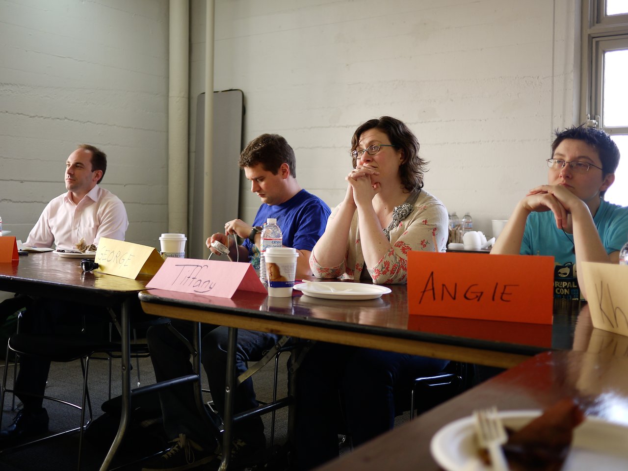 Four people sit at a table with name cards, listening attentively during a Drupal Association offsite meeting.