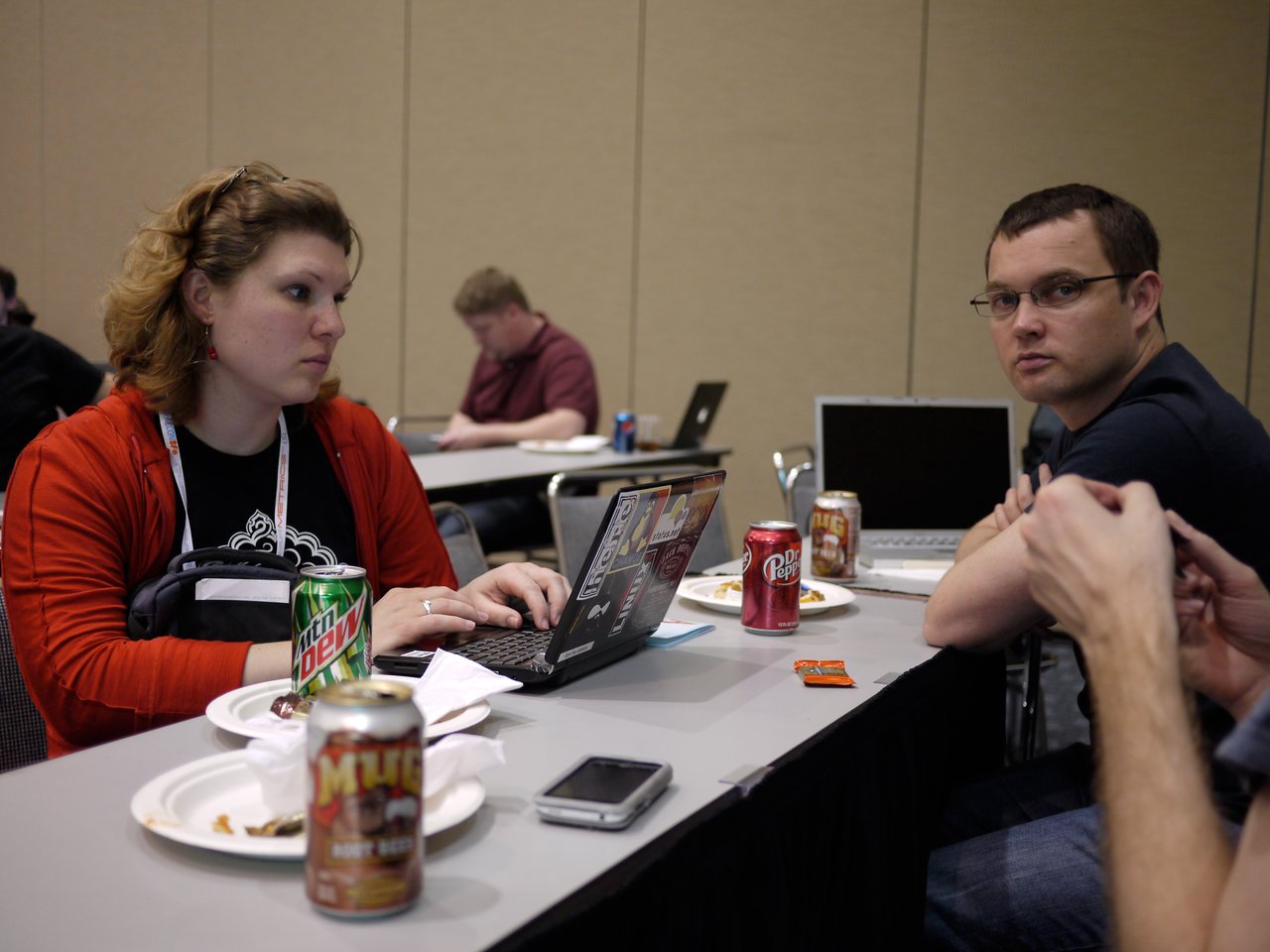A woman in a red sweater types on a laptop while talking with two people at a conference table.
