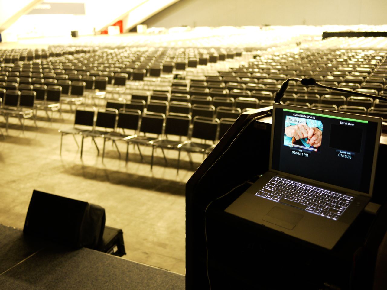 A laptop on a podium displays a "Thank you!" slide, overlooking an empty conference hall after a keynote speech.