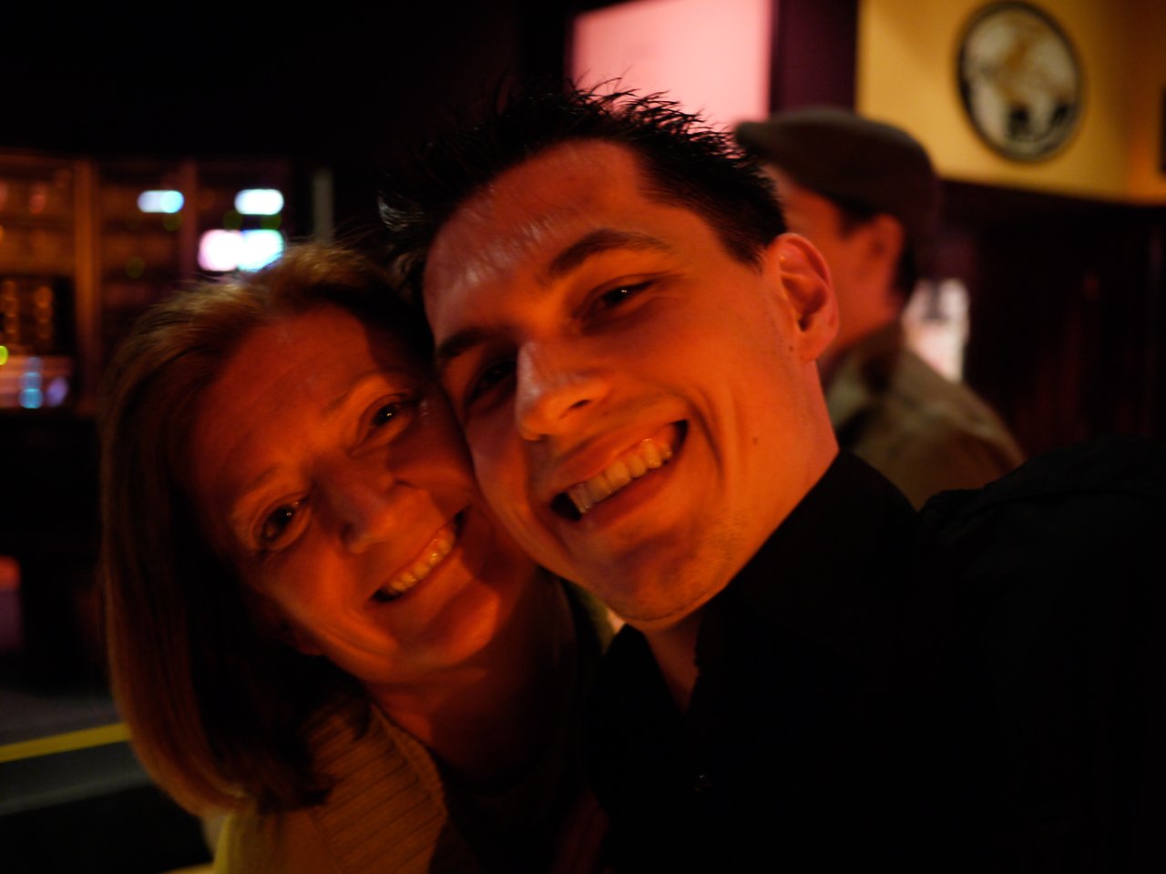 Two people smiling closely for a selfie in a dimly lit indoor setting.