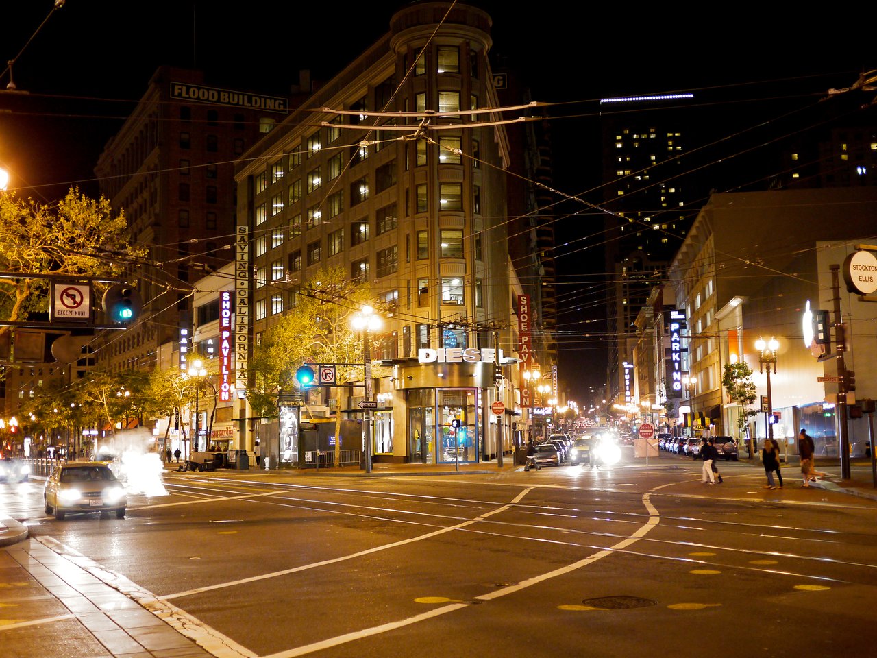 A busy San Francisco street at night with cars, pedestrians, and illuminated storefronts.