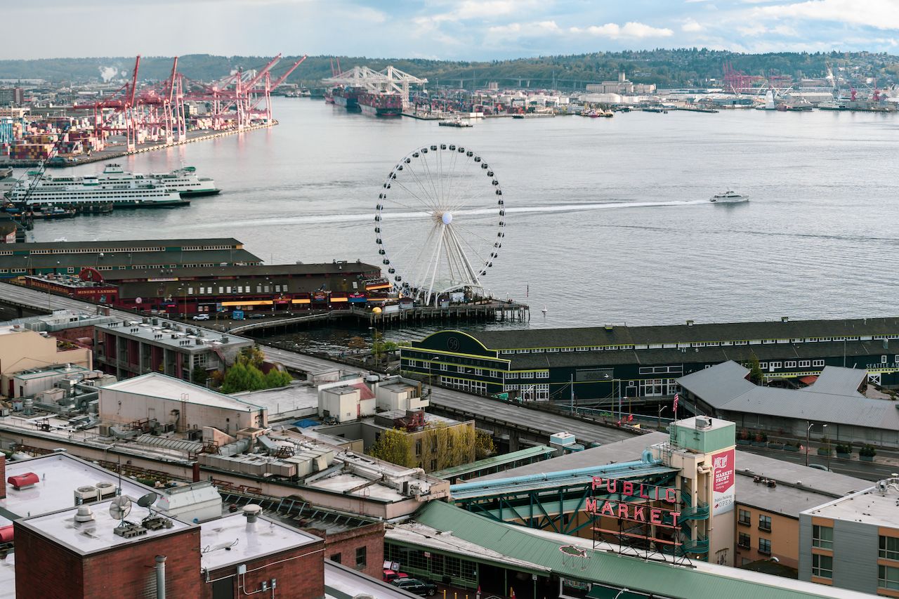A large Ferris wheel stands on a pier by the water, with boats and a market sign nearby.