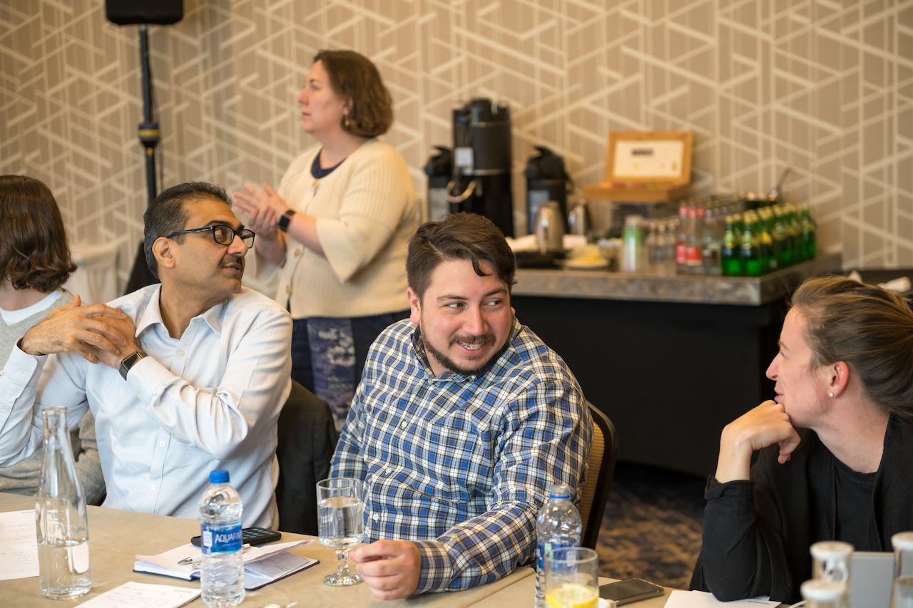 A group of people sit at a table, talking and listening.