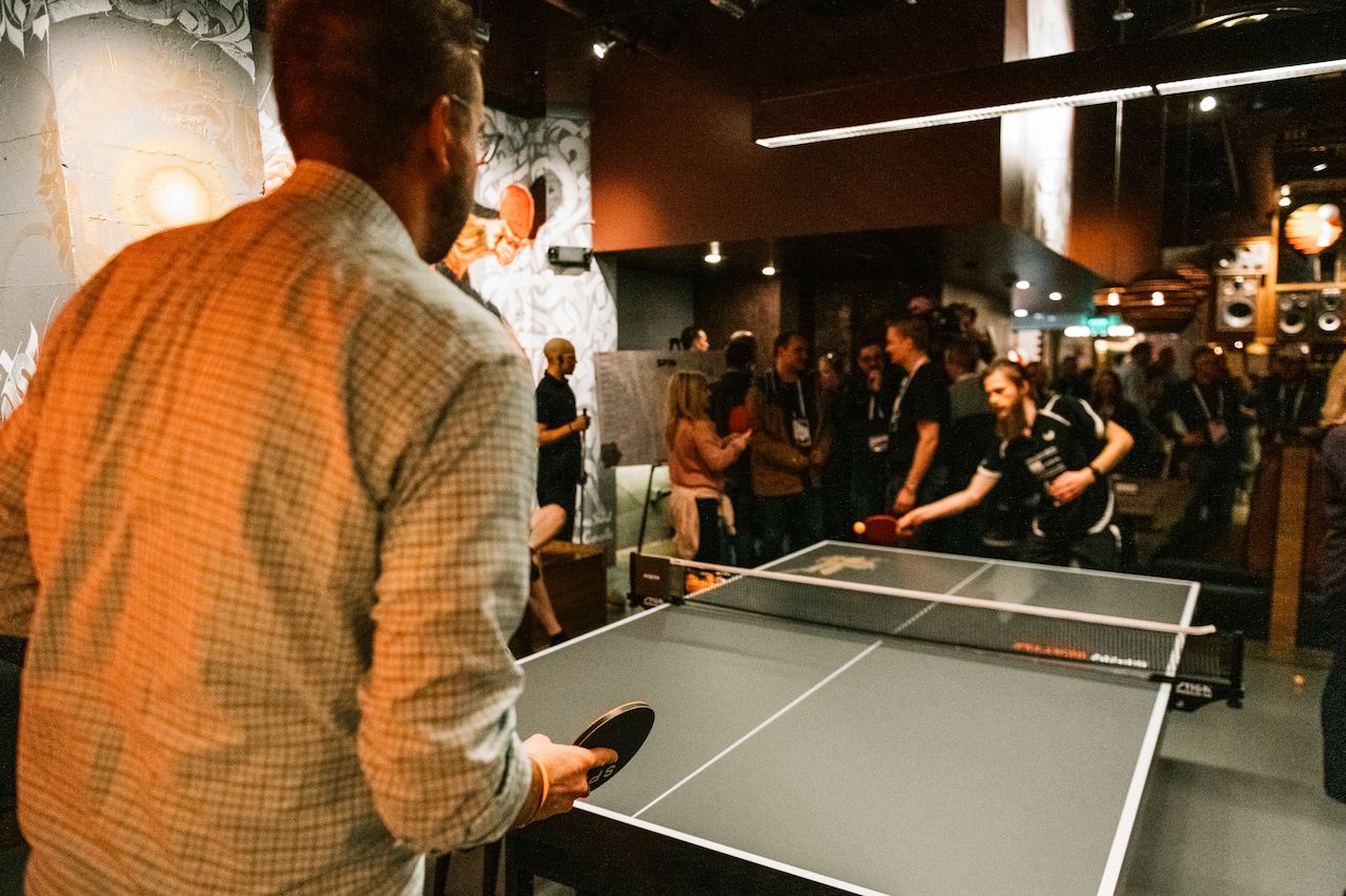Two people play a game of table tennis in a crowded bar.