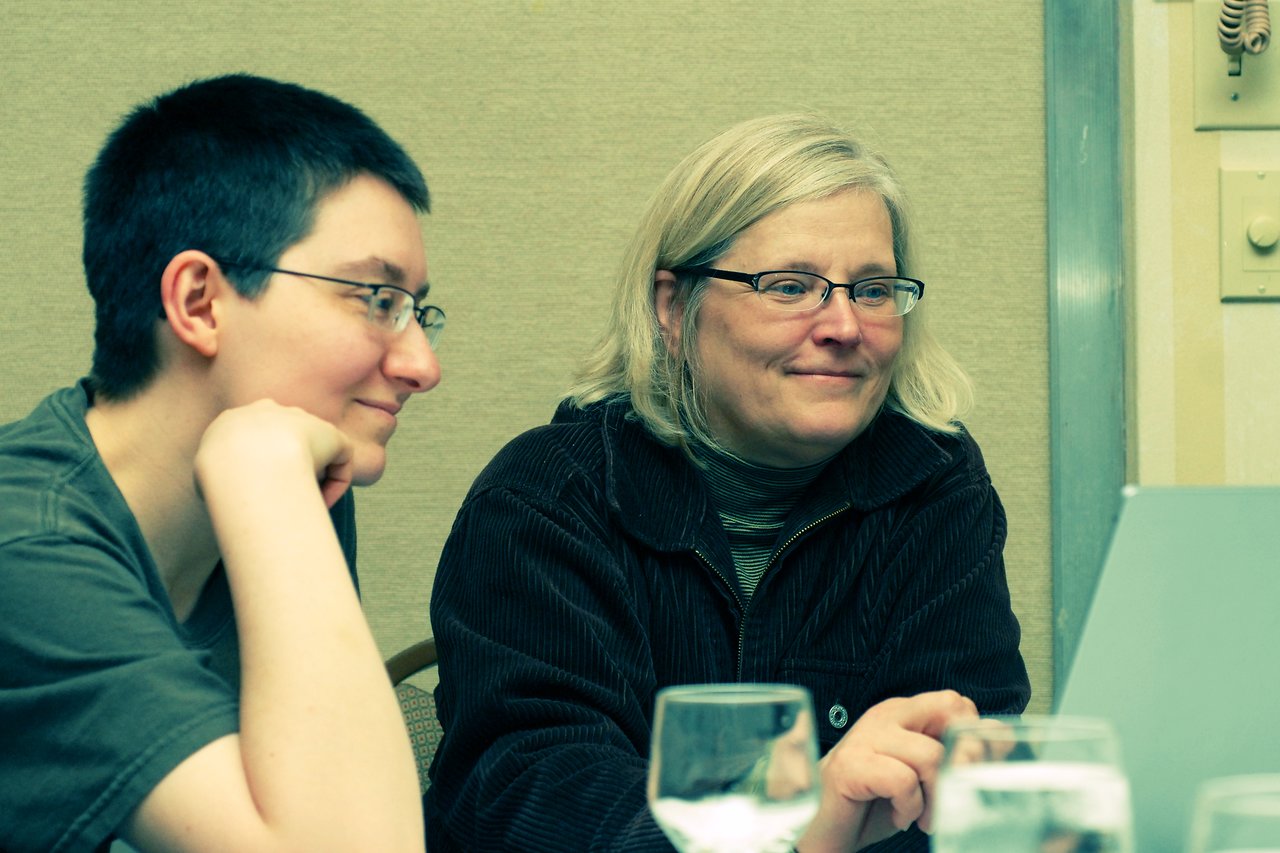 Two people sitting together, smiling and looking at a laptop screen in a conference setting.