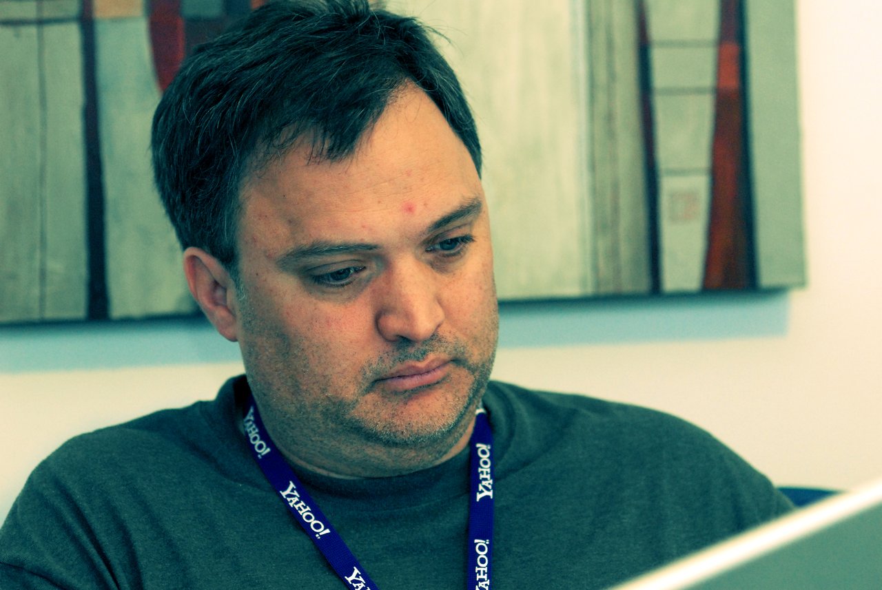A man wearing a Yahoo! lanyard looks at a laptop screen with a focused expression.