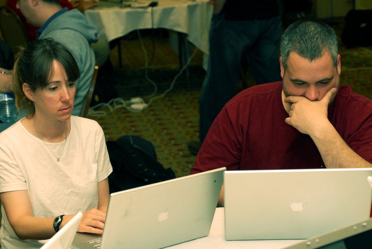Two people sitting at a table, focused on their laptops, working or collaborating at a conference.