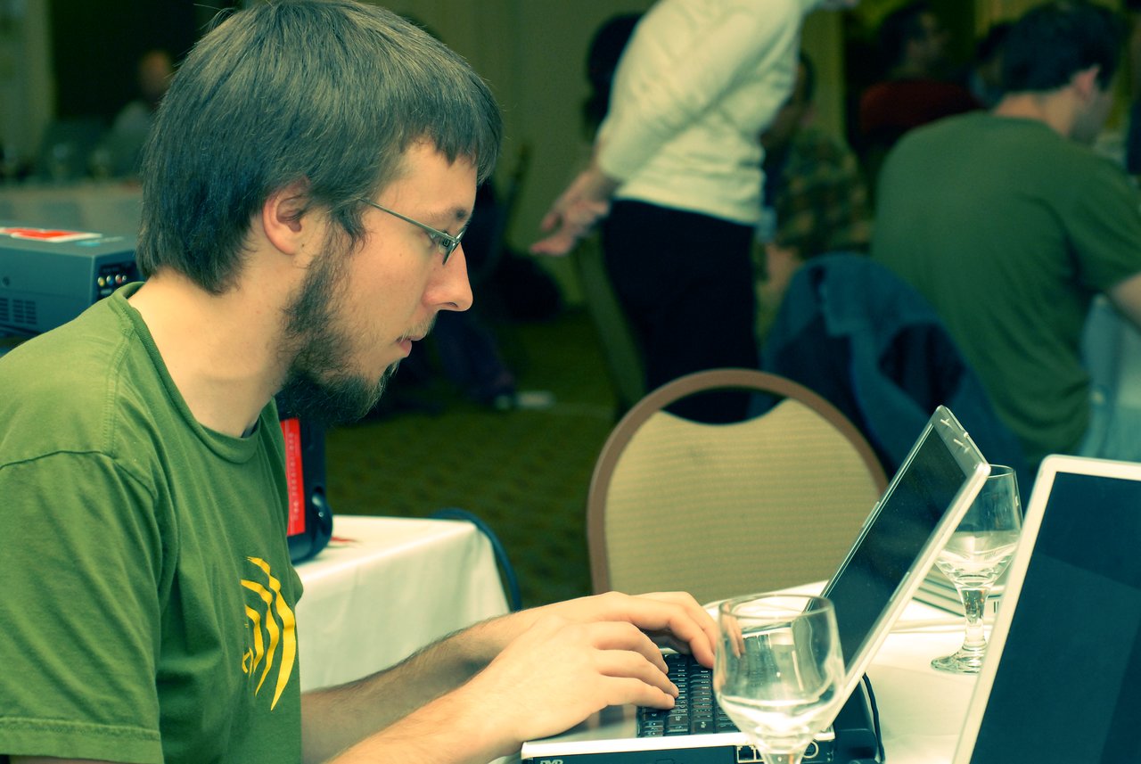 A man in a green shirt types on a laptop at a conference, focused on his work.