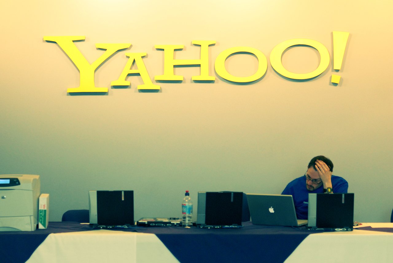 A staff member at the registration desk works on a laptop under a large Yahoo! sign.