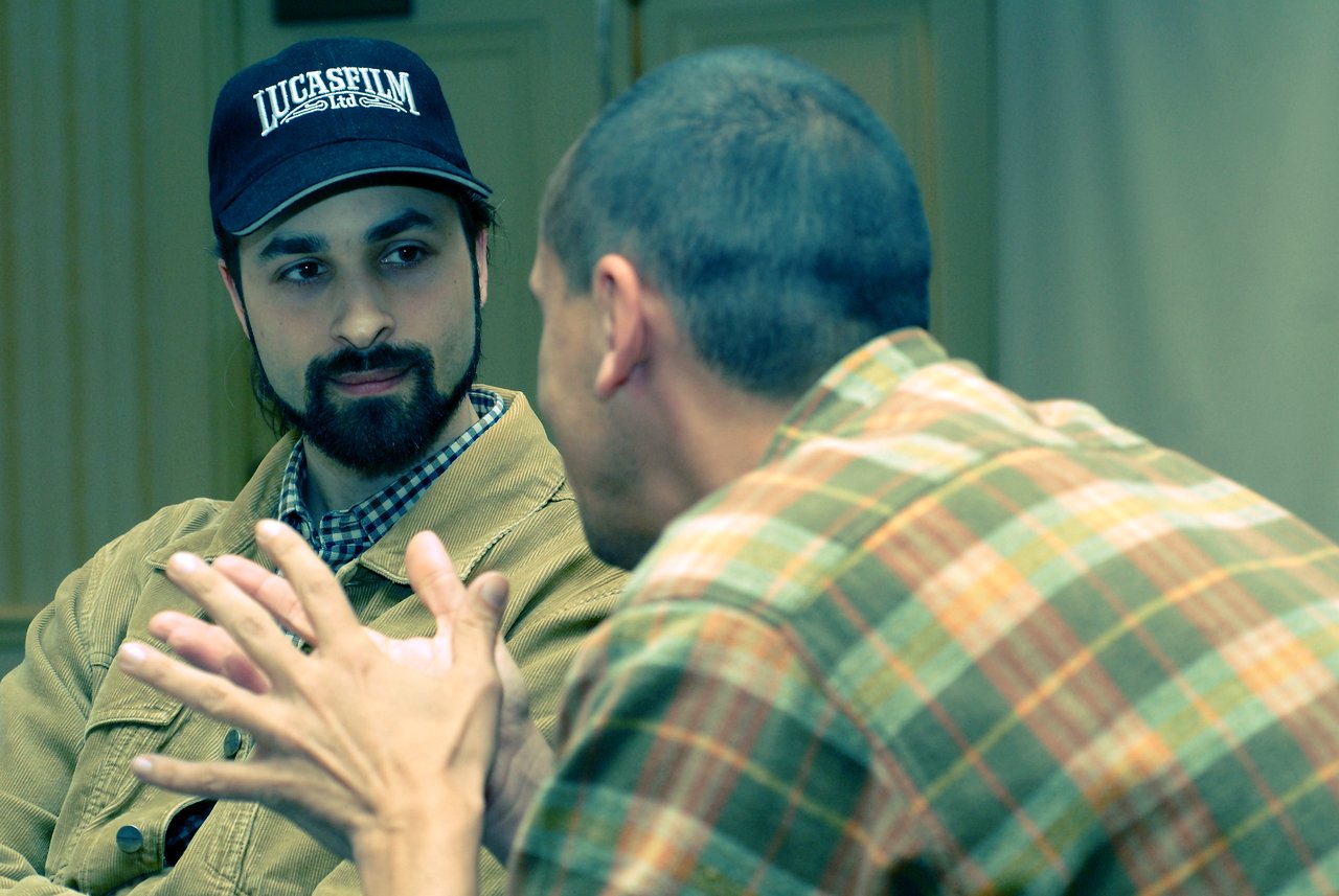 Two people engaged in conversation, one gesturing with hands while the other listens attentively.