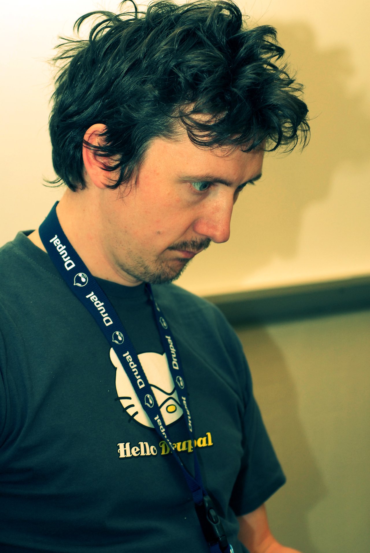 A person wearing a Drupal lanyard and t-shirt is focused on something in front of them.