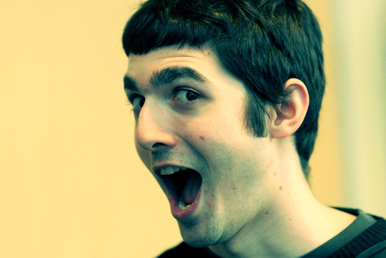 A person with short dark hair and a surprised expression, mouth open wide, looking slightly to the side.