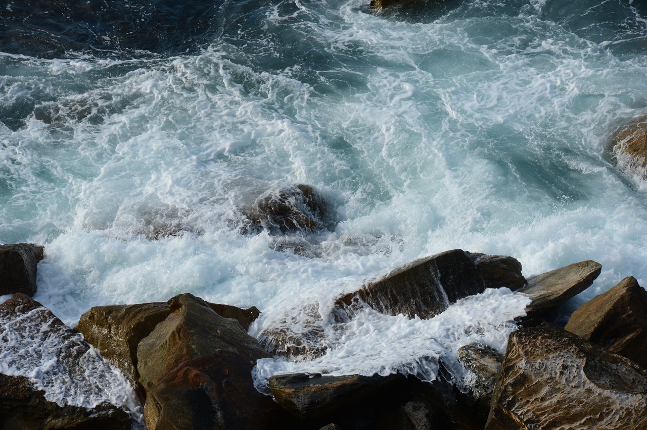 Waves crash against large rocks at Coogee Beach, creating white foam and splashes.