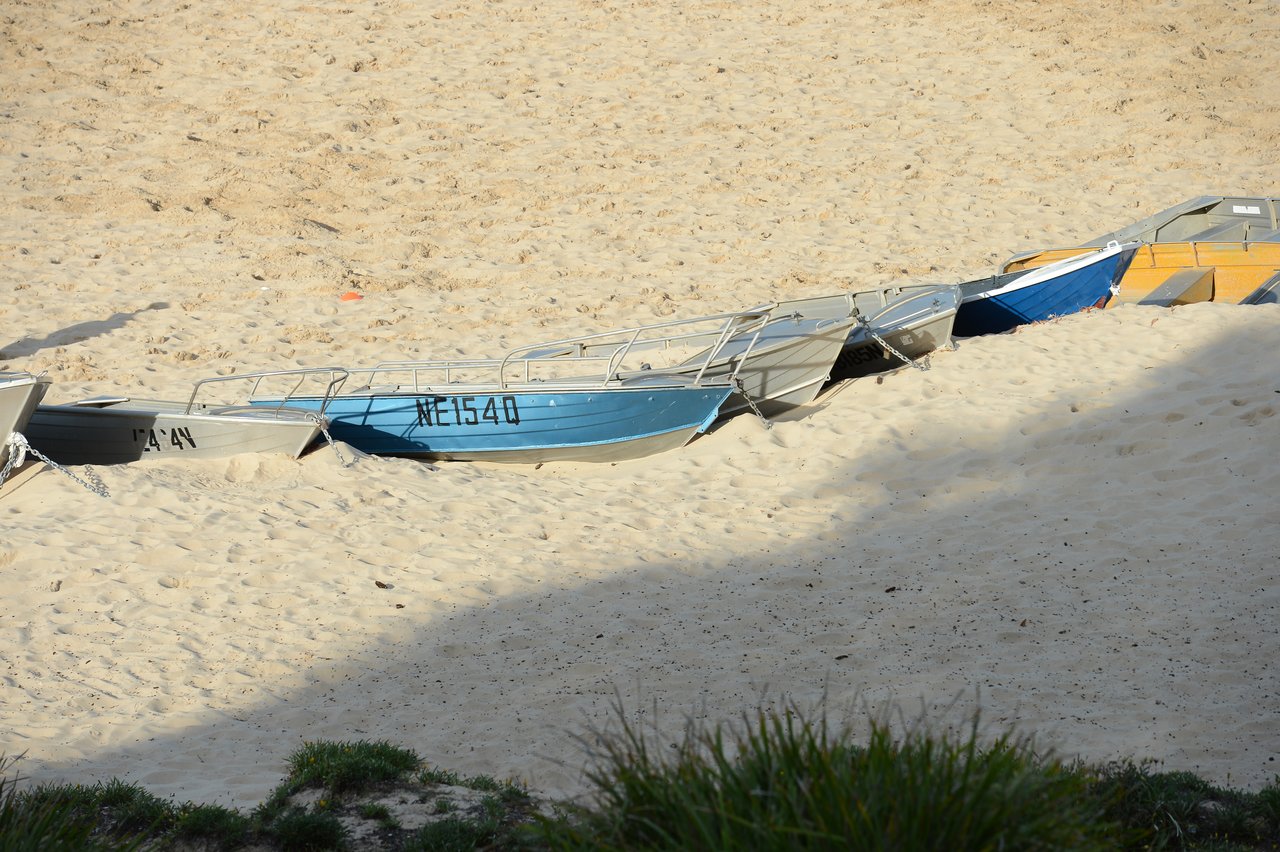 Several small boats rest on the sandy beach, lined up in a row with their hulls partially buried in the sand.