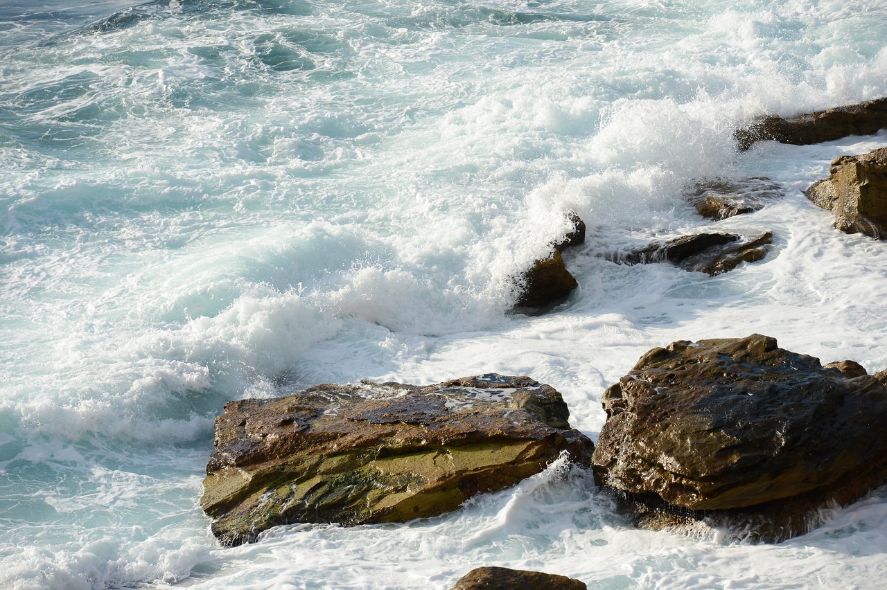 Waves crash against large rocks at Coogee Beach, creating white foam and splashes.