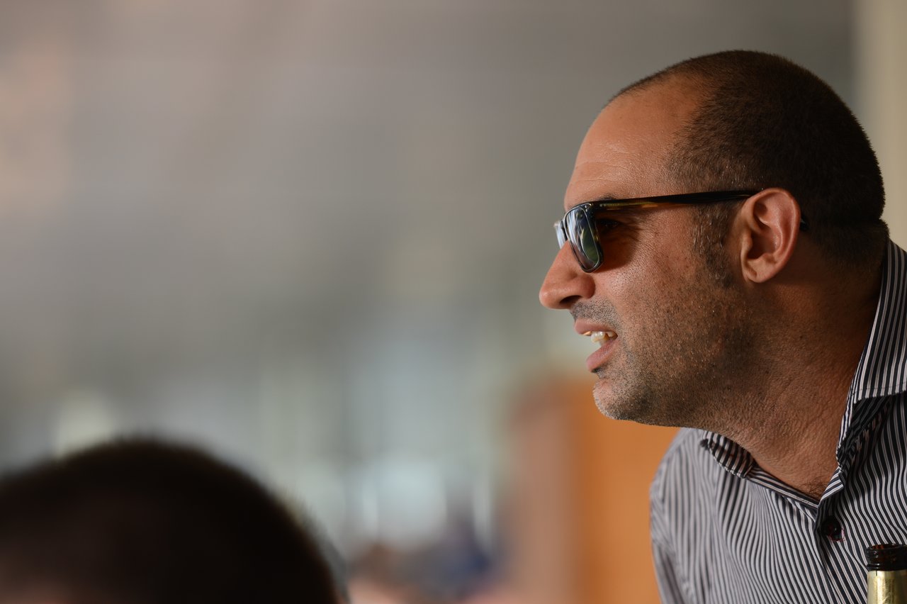 A man wearing sunglasses and a striped shirt leans forward, appearing to watch something intently.