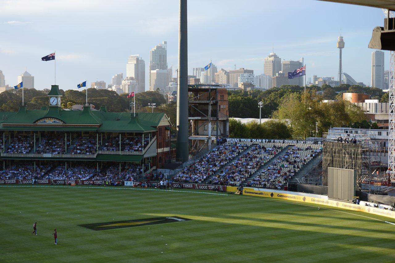 A cricket match in a stadium with a crowd watching, and two players standing on the field.
