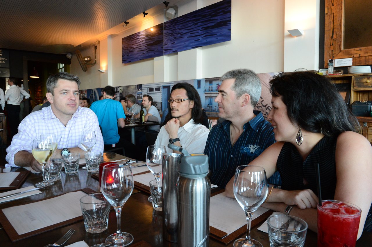 A group of four people sits at a restaurant table, engaged in conversation during DrupalCon Sydney 2013.